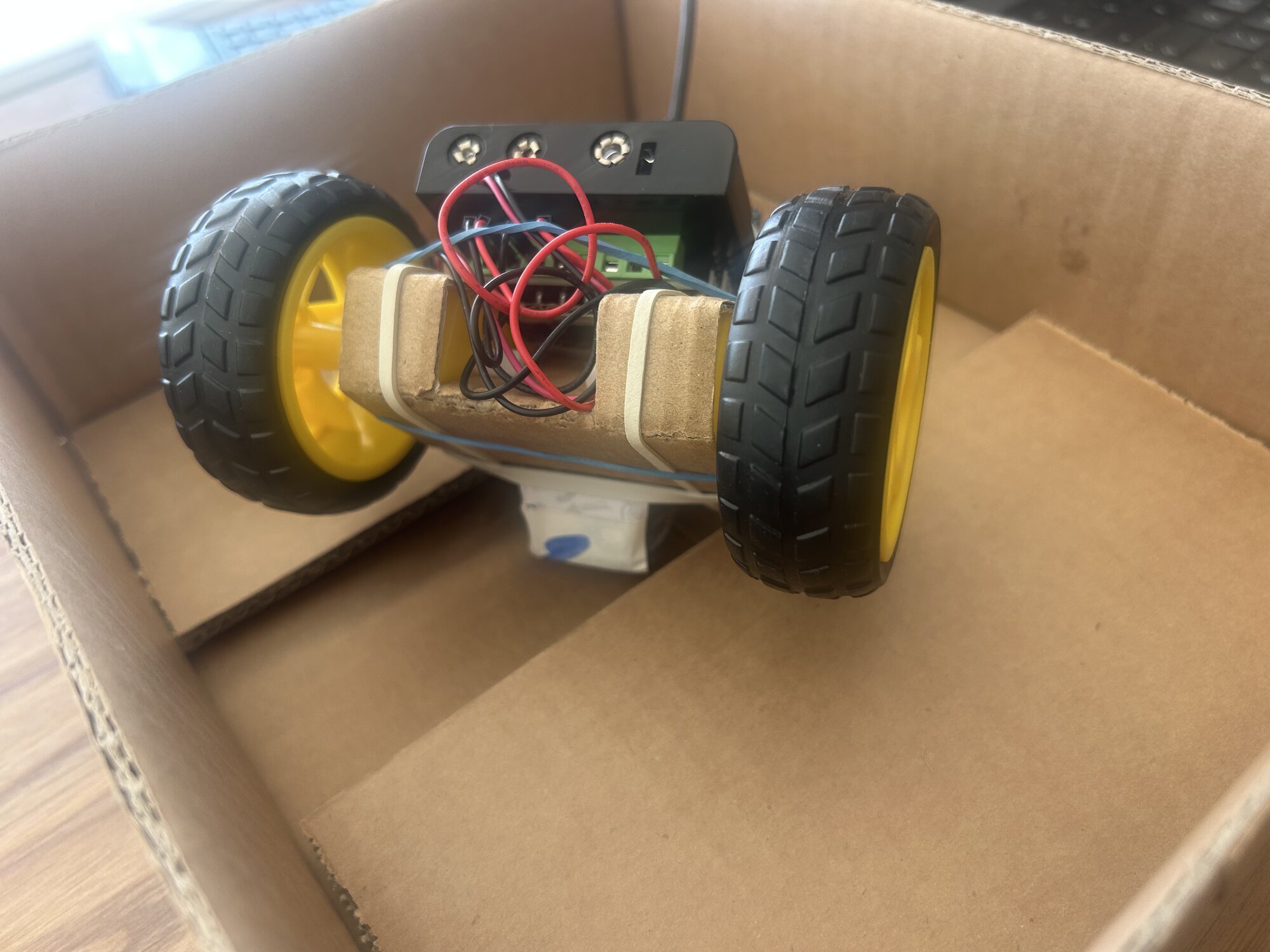 Le rover posé sur son pack d'accus, les deux roues en l'air, dans une boîte en carton